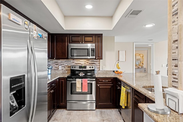 kitchen with decorative backsplash, light stone countertops, stainless steel appliances, and light wood-style floors