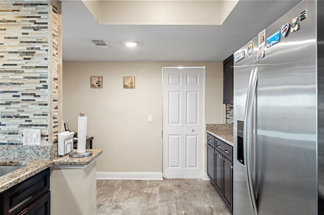 kitchen featuring stainless steel fridge with ice dispenser, visible vents, backsplash, and light stone counters
