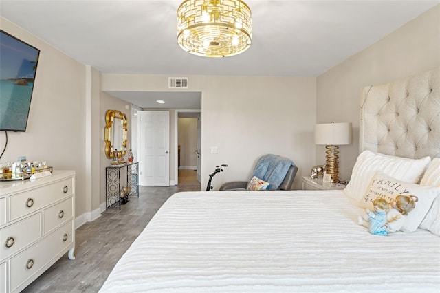 bedroom with wood finished floors, a notable chandelier, baseboards, and visible vents