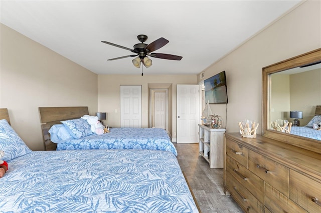 bedroom with multiple closets, visible vents, wood finished floors, and ceiling fan