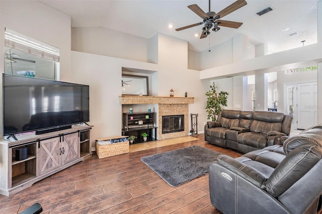 living room featuring wood finished floors, visible vents, high vaulted ceiling, a fireplace, and ceiling fan