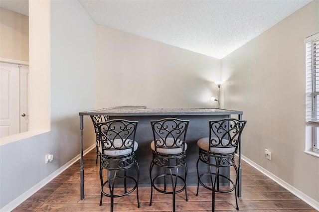 dining space featuring vaulted ceiling, a bar, baseboards, and wood tiled floor