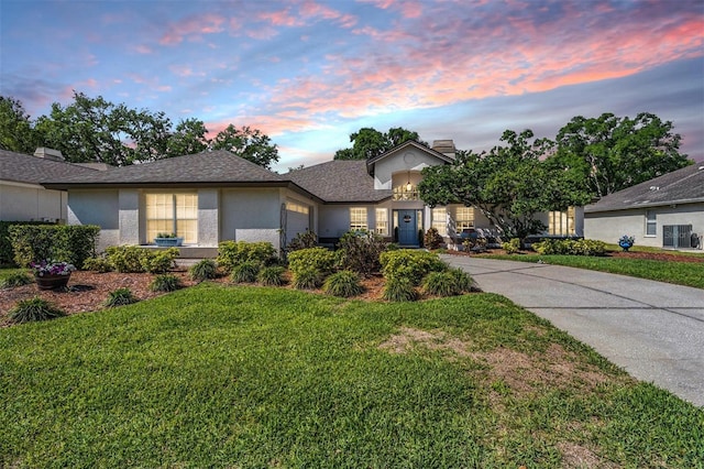 ranch-style home featuring stucco siding, driveway, a front lawn, an attached garage, and a shingled roof