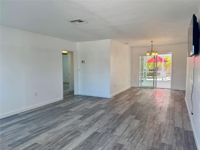 unfurnished room featuring visible vents, an inviting chandelier, baseboards, and wood finished floors