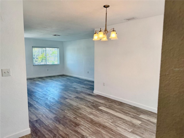 unfurnished room with baseboards, a notable chandelier, and dark wood finished floors