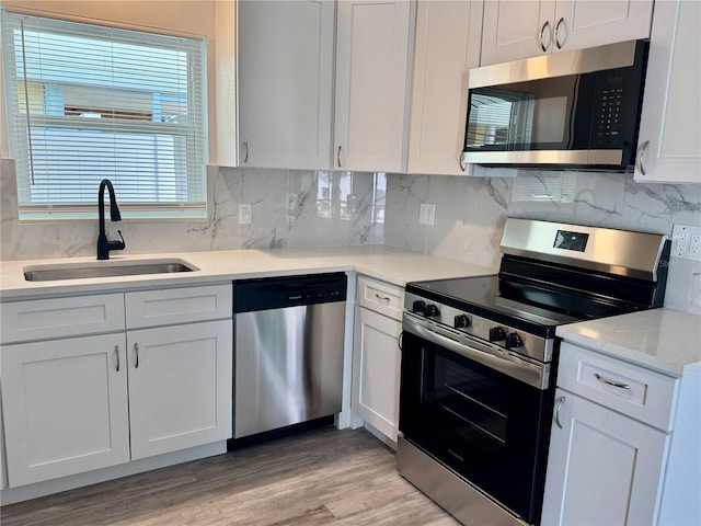 kitchen featuring light wood-type flooring, a sink, tasteful backsplash, white cabinetry, and stainless steel appliances