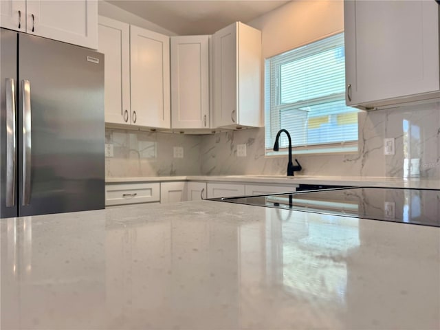 kitchen featuring light stone counters, tasteful backsplash, stainless steel refrigerator, and white cabinetry