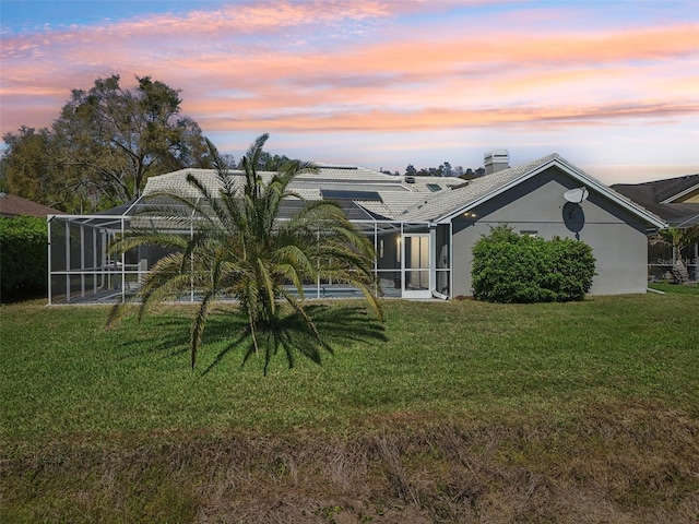 954 Cobblestone Ln, Tarpon Springs, FL 34688 - back of property at dusk featuring stucco siding, a chimney, a yard, and a lanai