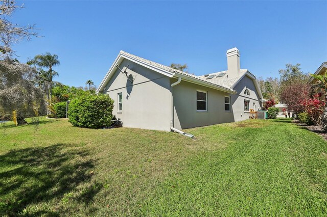 954 Cobblestone Ln, Tarpon Springs, FL 34688 - back of property featuring central air condition unit, a yard, stucco siding, and a chimney