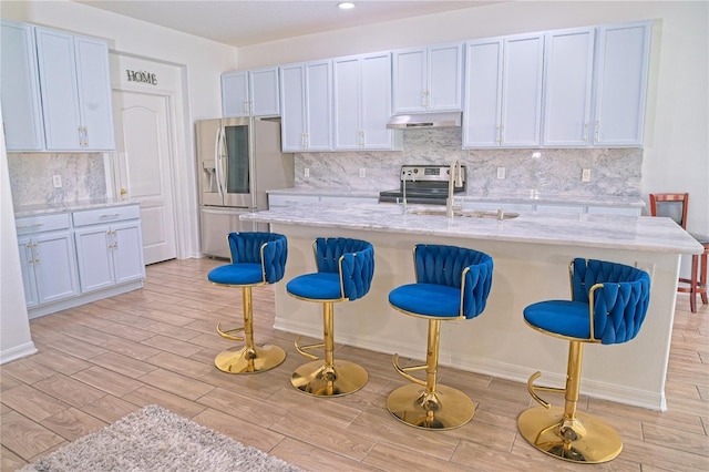 kitchen featuring a kitchen breakfast bar, tasteful backsplash, under cabinet range hood, light wood-style floors, and appliances with stainless steel finishes