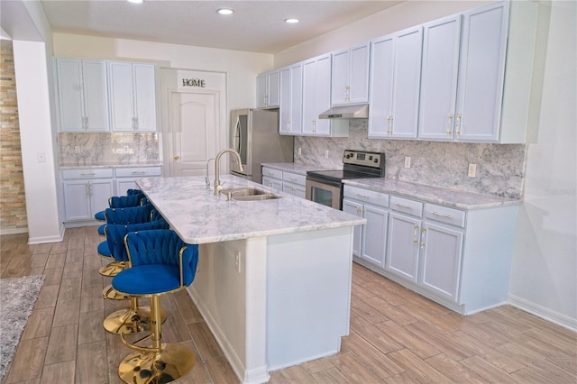 kitchen featuring light wood-type flooring, stainless steel appliances, under cabinet range hood, a breakfast bar, and a sink