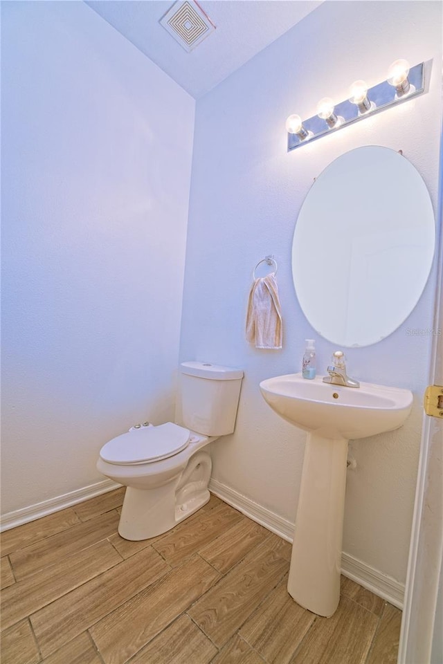 half bathroom featuring baseboards, visible vents, toilet, and wood finished floors