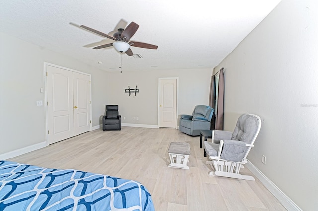 bedroom featuring baseboards, light wood-type flooring, visible vents, and a textured ceiling