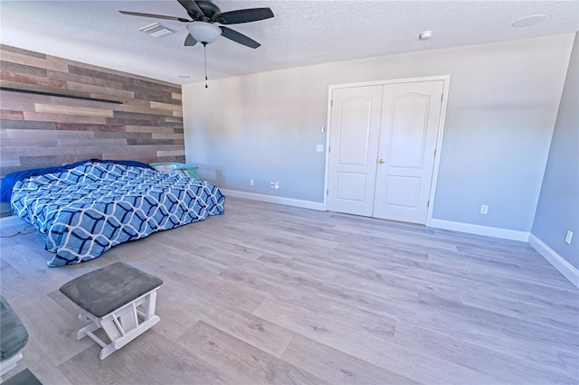 bedroom featuring wood walls, baseboards, an accent wall, a textured ceiling, and wood finished floors