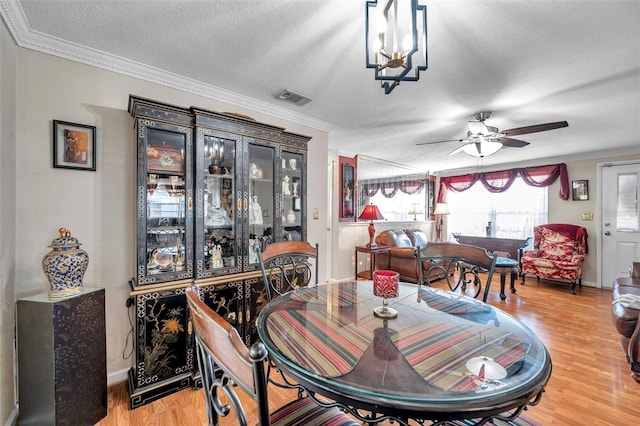 10035 Cherry Creek Ln, Port Richey, FL 34668 - dining area featuring visible vents, light wood-style flooring, a textured ceiling, crown molding, and ceiling fan with notable chandelier
