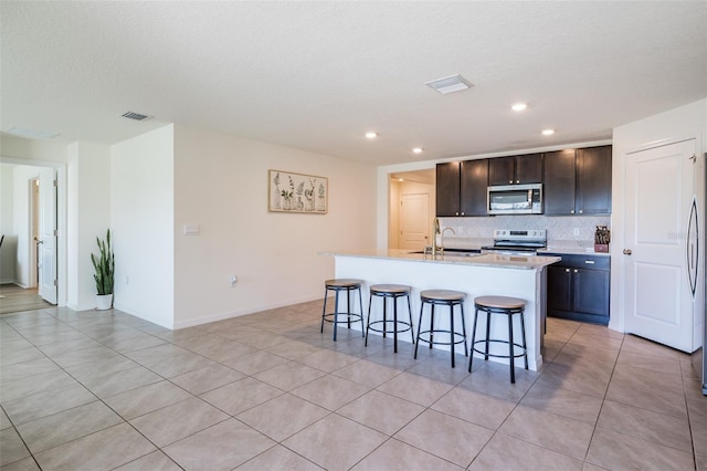 kitchen featuring visible vents, a kitchen island with sink, stainless steel appliances, a kitchen breakfast bar, and tasteful backsplash