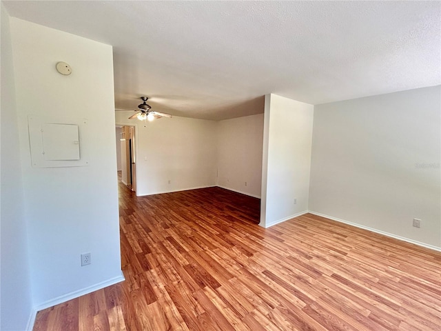 spare room with light wood-style flooring, a ceiling fan, baseboards, and a textured ceiling