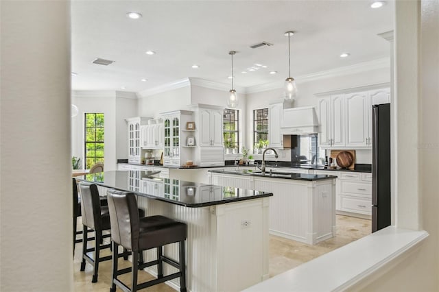 kitchen featuring dark countertops, visible vents, a center island with sink, freestanding refrigerator, and a sink