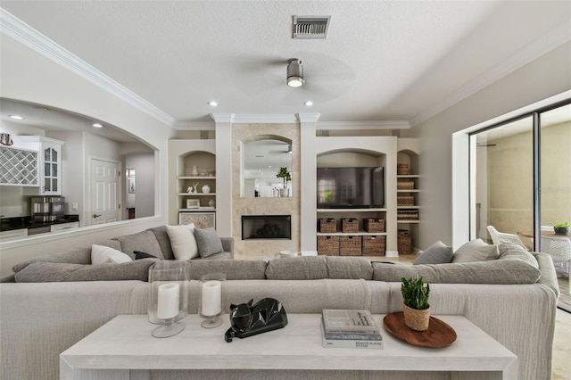 living room with visible vents, built in features, a textured ceiling, crown molding, and ceiling fan
