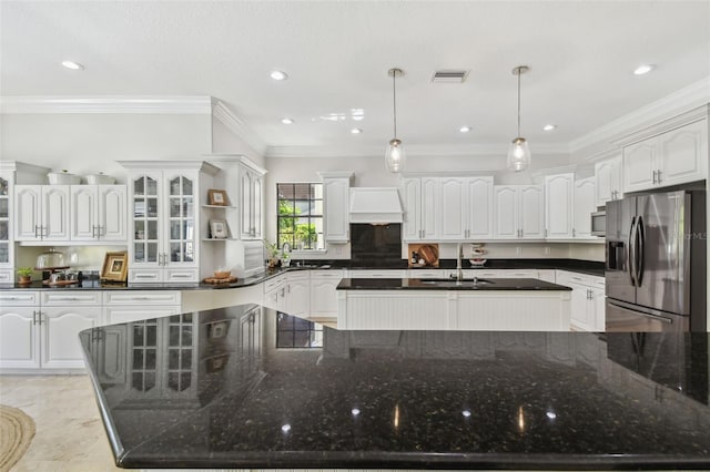 kitchen featuring a spacious island, crown molding, stainless steel refrigerator with ice dispenser, custom exhaust hood, and a sink
