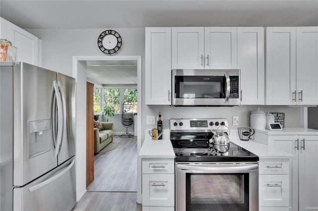 kitchen with appliances with stainless steel finishes, light wood finished floors, light countertops, and white cabinets