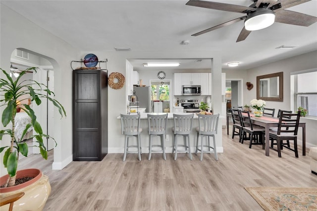 kitchen with a kitchen breakfast bar, white cabinets, stainless steel appliances, light wood-type flooring, and a peninsula