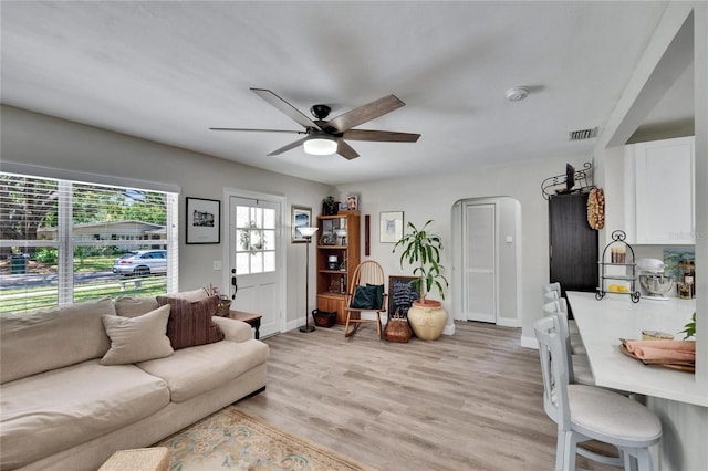 living area featuring light wood-style flooring, visible vents, arched walkways, baseboards, and a ceiling fan