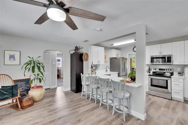 kitchen featuring arched walkways, light countertops, appliances with stainless steel finishes, and a kitchen bar