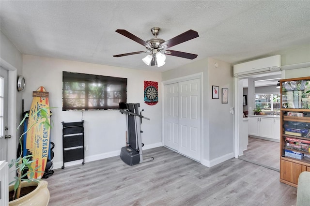 exercise area featuring light wood-style flooring, a textured ceiling, ceiling fan, and a wall mounted AC