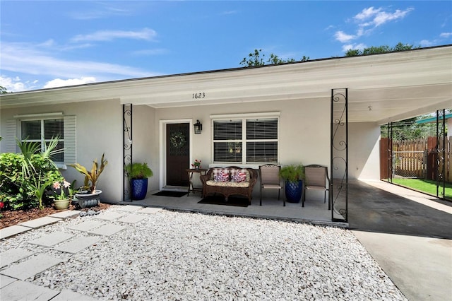 entrance to property with covered porch, fence, and stucco siding