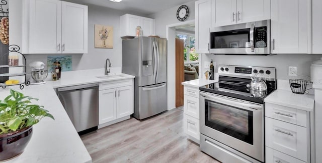 kitchen featuring light wood-style flooring, stainless steel appliances, light countertops, white cabinets, and a sink