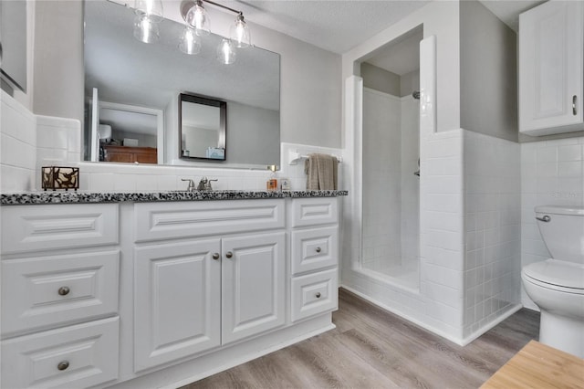 bathroom featuring toilet, wainscoting, tiled shower, and wood finished floors
