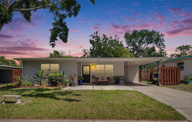 ranch-style home featuring a front lawn, an attached carport, concrete driveway, stucco siding, and fence
