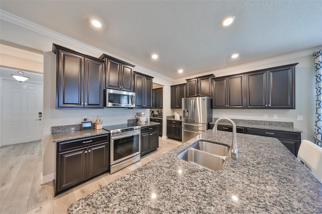kitchen featuring crown molding, dark stone countertops, light wood-style flooring, stainless steel appliances, and a sink