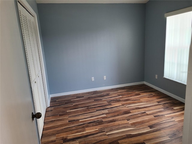 unfurnished bedroom with multiple windows, dark wood-type flooring, and baseboards