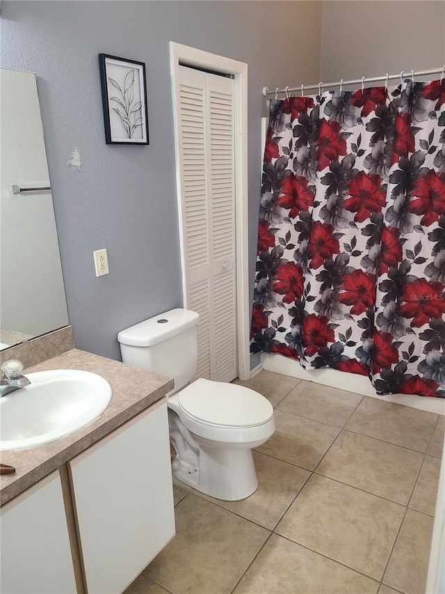 bathroom with a closet, vanity, tile patterned floors, and toilet