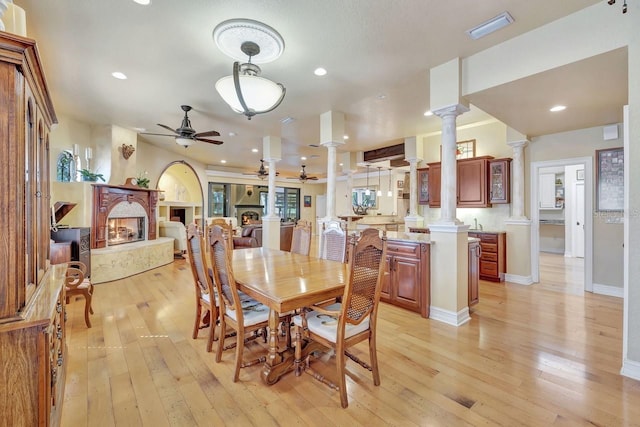 dining room featuring a ceiling fan, decorative columns, a lit fireplace, light wood finished floors, and baseboards