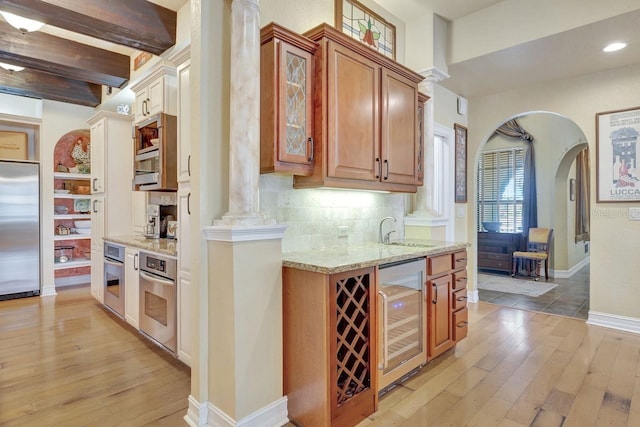 bar featuring appliances with stainless steel finishes, wine cooler, light wood finished floors, ornate columns, and decorative backsplash