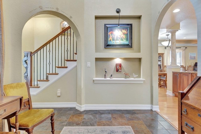 foyer featuring arched walkways, baseboards, dark stone finish floors, decorative columns, and stairs