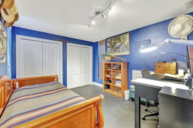 bedroom featuring a textured wall, multiple closets, and an office area
