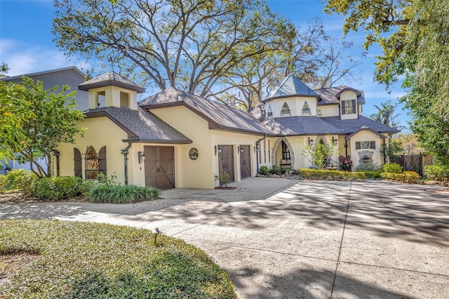 view of front of house featuring stucco siding, a garage, driveway, and fence