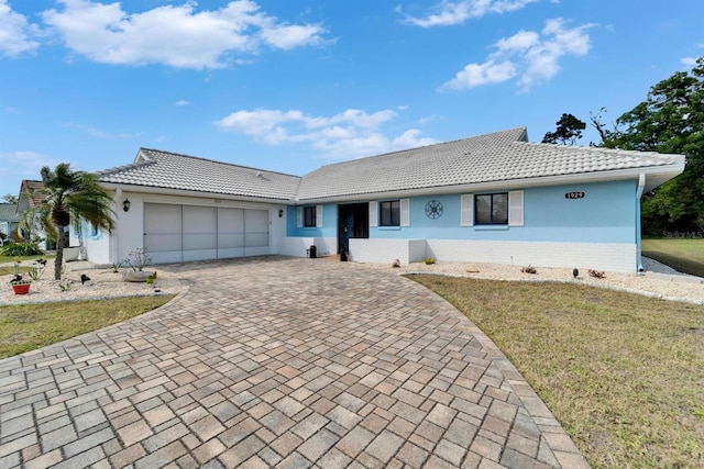 ranch-style home with stucco siding, a tile roof, decorative driveway, a front yard, and a garage