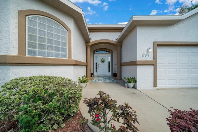 view of exterior entry with an attached garage and stucco siding
