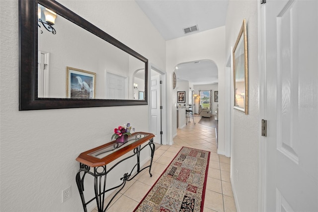 hallway featuring visible vents, arched walkways, baseboards, and light tile patterned flooring