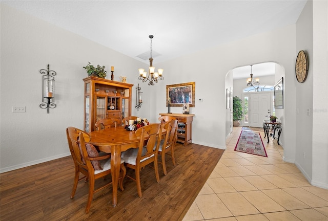 dining space featuring baseboards, arched walkways, an inviting chandelier, and light wood finished floors