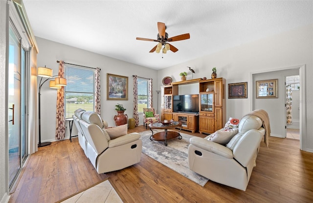 living area featuring a ceiling fan, baseboards, and light wood finished floors