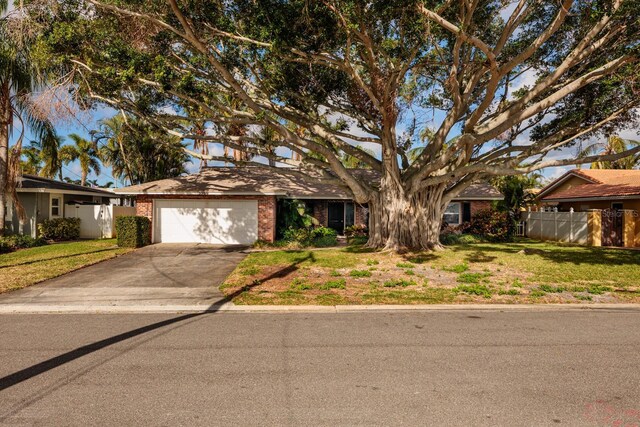 view of front of property featuring driveway, fence, an attached garage, brick siding, and a front lawn