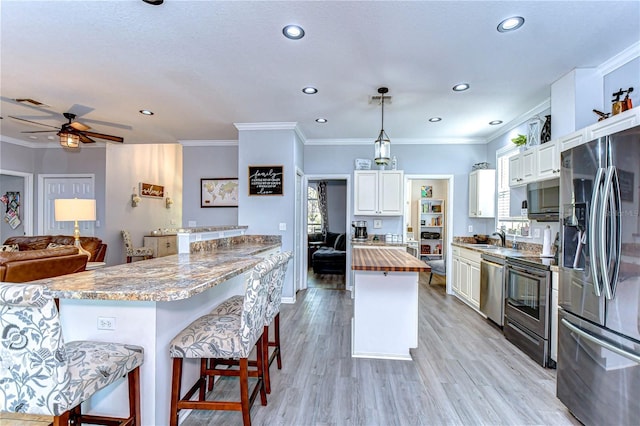 kitchen featuring butcher block countertops, crown molding, a ceiling fan, appliances with stainless steel finishes, and light wood-type flooring