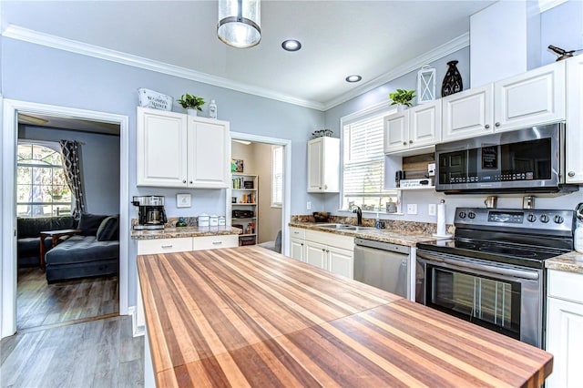 kitchen with wood counters, a sink, stainless steel appliances, and crown molding