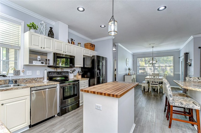 kitchen with a sink, white cabinetry, appliances with stainless steel finishes, a center island, and butcher block counters